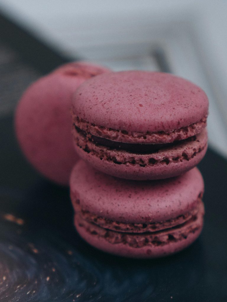 Close-up of pink macarons stacked on a black surface, highlighting their texture.