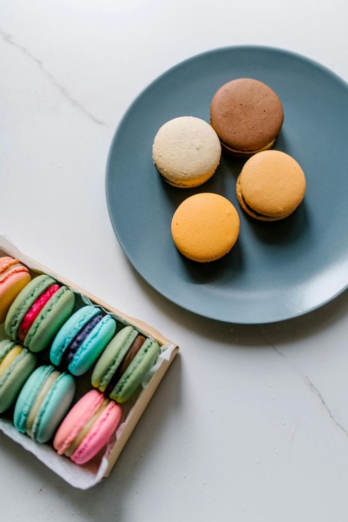 Vibrant French macarons arranged on a plate and in a box on a marble surface.
